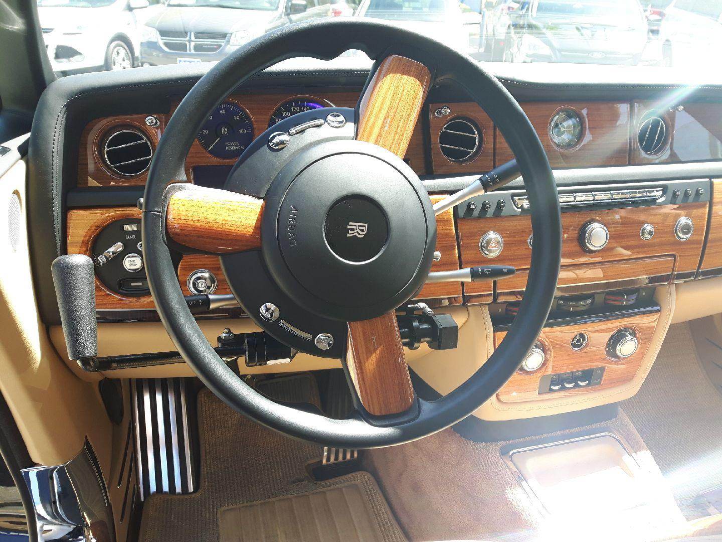 A push-pull hand control fitted to the steering column of a Rolls-Royce with a wood-trimmed dashboard, photographed on the lot in Gainesville.
