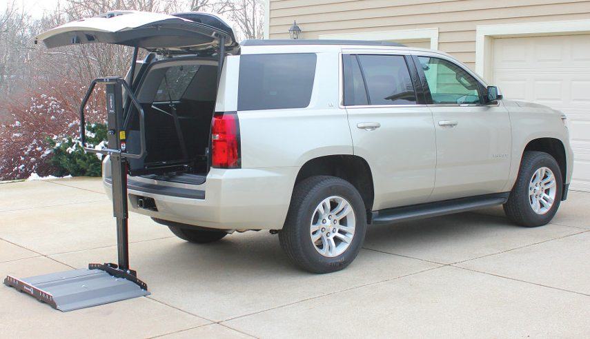 A powered lift installed inside an SUV's tailgate, arm extended over the driveway.