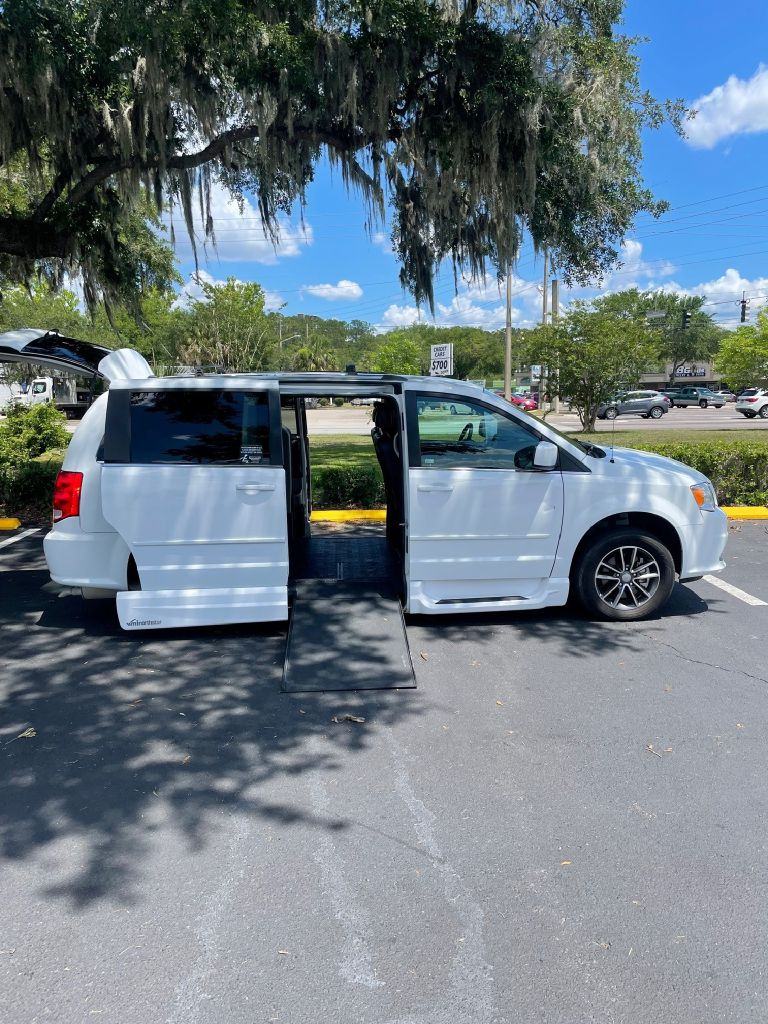 Full passenger-side view of the same van, side door open, ramp deployed onto the asphalt and rear hatch raised.